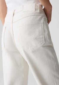 Witte spijkerbroek met een hoge taille, achterzakken, subtiele stiksels en een gestructureerde stof. Een merklabel is zichtbaar aan de achterkant.