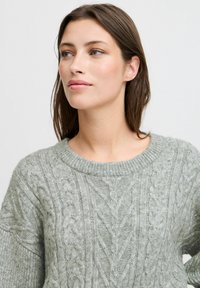 Hellgrüner Strickpullover mit einem Zopfmuster, runden Ausschnitt und lockerer Passform. Weiches Material mit detaillierter Musterung.
