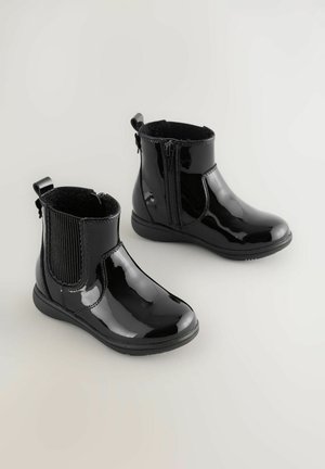 Stivaletti alla caviglia in vernice nera con una finitura liscia, pannelli laterali elasticizzati e chiusura con zip. Presentano una suola in gomma a basso profilo e texturizzata.