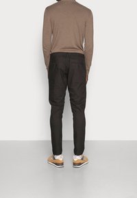 Pantaloni neri aderenti, realizzati in cotone. Presentano una cintura con coulisse e due tasche posteriori, abbinati a sneakers marroni.