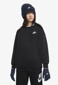 Crna dukserica s bijelim Nike logom, uparena s tamnoplavim rukavicama i kapom. Glatka tkanina, širok kroj i kontrastni color akcenti.