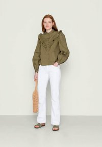 Blusa verde-oliva com detalhes em folhos, frente com botões e mangas bufantes, combinada com calças brancas à boca de sino e sandálias verdes.