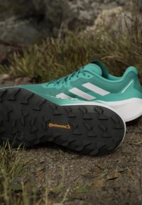 Scarpe sportive color teal con strisce bianche, suola in gomma testurizzata e logo Continental. Progettate per offrire trazione su terreni variabili.