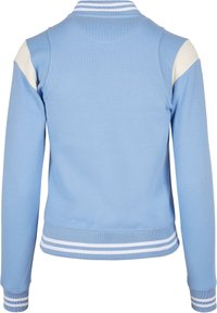 Ljusblå långärmad jacka med vita axelaccenter, ribbat krage, cuffs och nederkant som har vita dubbla ränder, visad bakifrån.