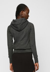 Sudadera oscura gris para hombre con un bolsillo frontal, puños y dobladillo acanalados, que presenta una capucha con cordón y una tela suave con textura.