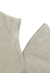 Tissu beige clair avec une surface douce et texturée. Présente un zip et des bords lisses, mettant en avant un design simple et fonctionnel.