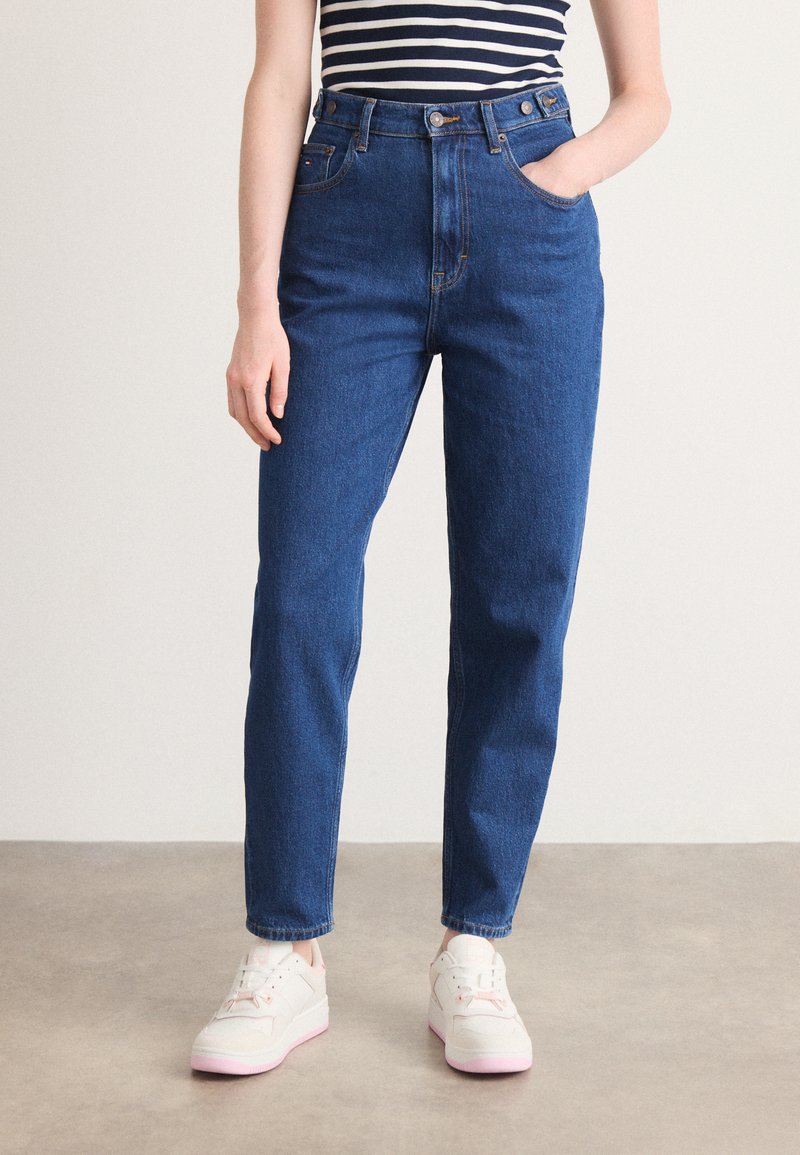 Høyt midje blå jeans laget av denim med rett passform, fem-lomme-design og knappelukking foran, kombinert med hvite joggesko.