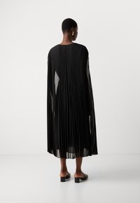 Black pleated dress with long sleeves, sheer fabric, and a flowy silhouette. Worn with black block-heeled sandals. Elegant texture and design.
