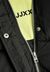Černá zateplená bunda má stříbrný zip a patentky. Uvnitř je jasně žlutá podšívka se zobrazením nápisu "JJXX" v černém písmu. Texturovaná tkanina, prošívaný design.
