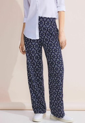Pantalons larges à motifs en bleu foncé avec un design géométrique en bleu clair et blanc. Fabriqués en tissu léger, assortis à des baskets blanches.