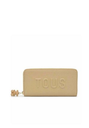 Cartera rectangular beige con texto en relieve "TOUS" y un pequeño tirador de cremallera en forma de oso en el lado izquierdo.
