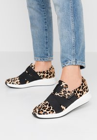 Sneakers med leopardprint og sorte elastikstropper, rund tå, polstret hvid sål og tekstureret overdel. Jeans med opsmøgbar kant synlig.