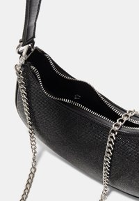 Črna torbica z teksturirano površino in srebrno verižico kot trak. Ima zadrgo na vrhu in notranji žep ter se ponaša z elegantno, ukrivljeno zasnovo.