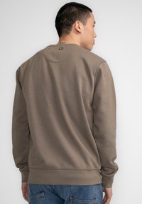 Bruine crewneck sweatshirt gemaakt van zachte stof. Bevat ribgebreide zomen en manchetten, met een klein logo label aan de achterkant van de halslijn.