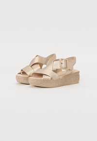Gold metallic sandals with crisscross straps, a large buckle, and a woven platform sole. Smooth texture with a lightweight design.