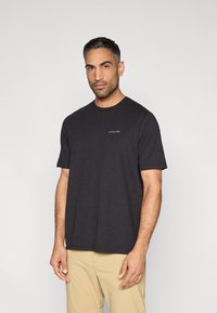 Čierne tričko s krátkym rukávom z bavlny, vybavené okrúhlym výstrihom a malým logom na ľavej strane hrudníka. Hladká textúra s voľným strihom.