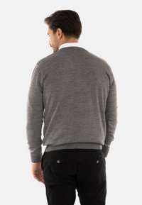 Maglione grigio a maglia con maniche lunghe, dotato di scollo a girocollo. Il tessuto appare morbido, indossato sopra pantaloni neri con tasche posteriori con bottoni.