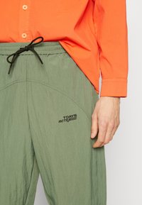 Zielone spodnie sportowe z teksturowanym wykończeniem, elastycznym paskiem w talii i sznurkiem do regulacji. Na udzie znajduje się czarne logo "7 DAYS ACTIVE".