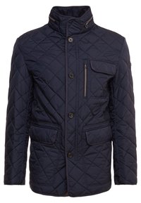 Granatowa, pikowana kurtka z wysokim kołnierzem, z przodu zapinana na guziki, z kieszenią na suwak oraz dwiema kieszeniami naszytymi; charakteryzuje się kontrastowym przeszyciem i teksturowanym wykończeniem.