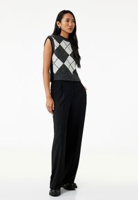 Suéter sin mangas de argyle en tonos gris y blanco, combinado con pantalones negros de alta cintura. Textura suave, diseño minimalista, sin patrones visibles.