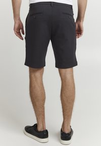 Shorts noirs avec une coupe ajustée, dotés de poches avant et arrière, et d'un tissu lisse. Comprend des boutons discrets sur les poches arrière.