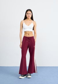 Bordeaux sweatpants med bred bendesign, hvide sideløse striber, guld accenter og drawstring talje. Sammen med en tætsiddende hvid crop top.