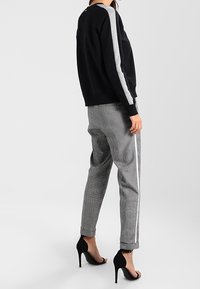 Sweatshirt noir avec des rayures latérales grises, associé à un pantalon gris à motifs. Le pantalon a des accents latéraux blancs. Modèle portant des talons noirs.