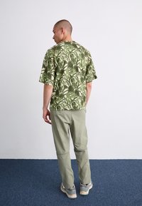 Short-sleeved green shirt with a botanical pattern, paired with light green pants. The outfit features a relaxed fit and soft fabric texture.