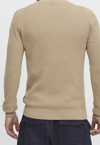 Beżowy sweter dziany z teksturowanej tkaniny, z długimi rękawami, ściągaczami przy mankietach i dolnym obszyciu, z okrągłym dekoltem i dopasowanym krojem.