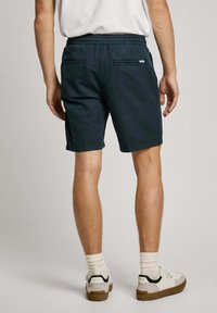 Pantalones cortos de color verde oscuro hechos de una tela ligera, con una cinturilla elástica, dos bolsillos en la parte posterior y dobladillos enrollados.