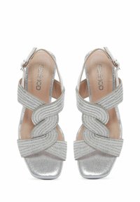 Sandales à talons argentées avec un large strap tressé, finition brillante et bout carré. Fermeture à boucle sur la bride de cheville.