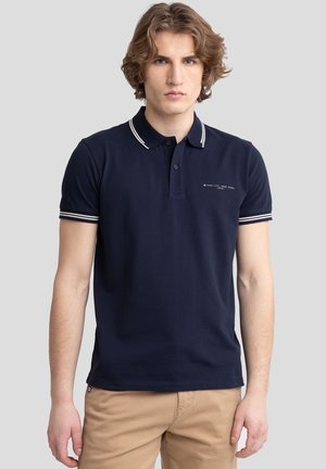 Camisa polo de color azul marino con cuello y detalles en las mangas a rayas blancas, hecha de algodón, con un pequeño logo en la zona del pecho.