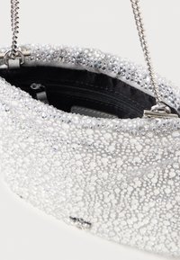 Silberene Handtasche, verziert mit Strasssteinen, mit schwarzem Innenleben und Kettenriemen. Nahaufnahme zeigt die strukturierte Oberfläche und den Reißverschlussdetails.