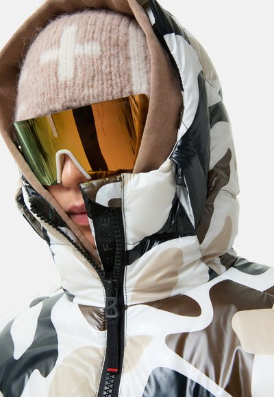 Gevoerde camouflage pufferjack in zwart, wit en bruin. Beschikt over een hoge kraag, ritsluiting en een gestructureerde stof. Gepaard met oversized zonnebrillen.