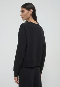 Felpa nera con vestibilità ampia, collo a giro ribattuto e polsini. Texture liscia con orlo corto sul retro.