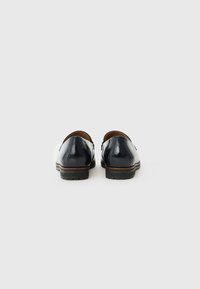 Mocassins en cuir marine avec une finition brillante, bout rond, accents en cuir marron contrastés, et semelle en caoutchouc texturée. Détails de couture visibles.