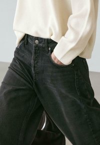 Jeans in denim nero dal taglio dritto, con cinque tasche e chiusura con bottone metallico. Abbinati a un maglione color crema. Tessuto lavorato.