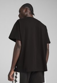 T-shirt noir oversize en coton, avec des manches courtes et un col rond sans coutures, vu de l'arrière.