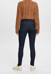 Vaqueros skinny azul oscuro con una cintura alta, combinados con un suéter de punto marrón texturizado. Cuenta con bolsillos traseros y un acabado suave.