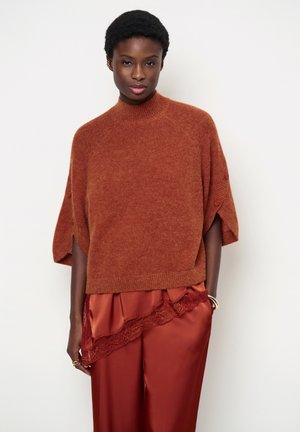 Woman wearing a rust-colored short-sleeve sweater and matching satin pants with lace trim, standing against a plain white background.