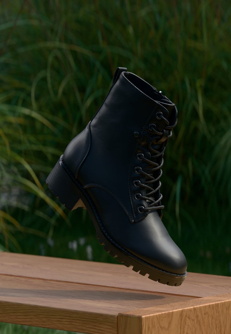 Botte noire en cuir à lacets suspendue au-dessus d'une surface en bois avec de l'herbe verte floue en arrière-plan.