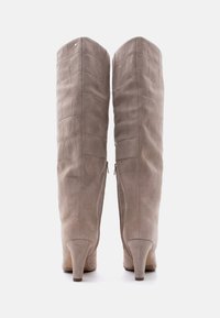 Μπότες από σουέντ σε ταουπέ χρώμα μέχρι το γόνατο με διακριτικό σχέδιο κροκόδειλου, φερμουάρ στο πίσω μέρος και μεσαίου ύψους τακούνια σε λευκό φόντο.