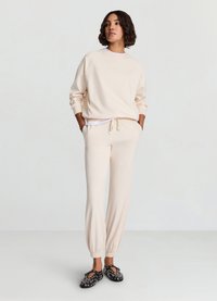 Sweat-shirt beige clair avec manches raglan, assorti d'un pantalon de survêtement fuselé. Mocassins noirs avec accents argentés. Texture lisse.