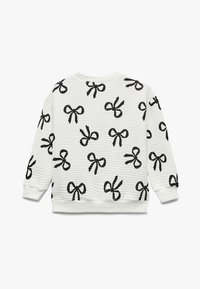 Suéter de manga larga blanco con textura de canalé y patrones de lazo negro distribuidos uniformemente por toda la tela.