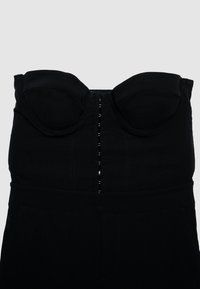 Tuta nera senza spalline con coppe strutturate, chiusura centrale con gancio e cuciture verticali, realizzata in tessuto liscio con finitura opaca.