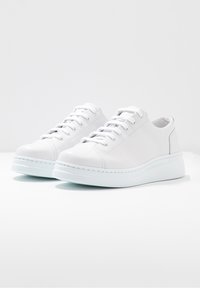 Zapatillas blancas de cuero con textura suave, diseño con cordones, punta redondeada y suela gruesa de goma blanca. Sin patrones ni logotipos visibles.