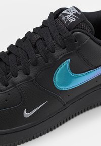 Svarta Nike Air Force 1-sneakers i texturerat läder, svarta snören och en iriserande blå Nike-swoosh på sidan.
