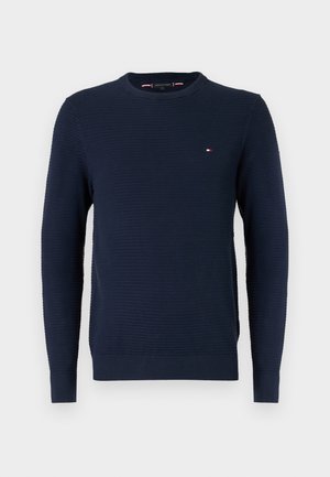 Dunkelblaues, geripptes Strickpullover mit Rundhalsausschnitt und langen Ärmeln sowie kleinem roten, weißen und blauen Logo auf der linken Brust.