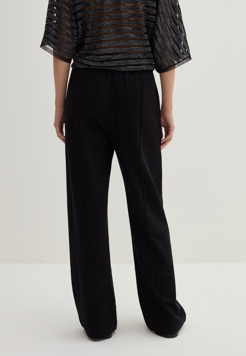 Schwarze, weit geschnittene Hosen aus weichem Material mit glatter Textur. Mit hohem Bund und dezentem Nahtdetails.