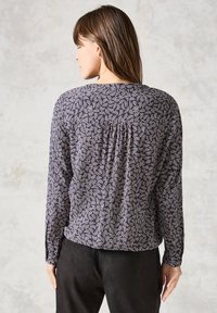 Blusa a maniche lunghe in navy con motivo astratto bianco, presenta un dettaglio arricciato sul retro. Tessuto morbido, vestibilità comoda.